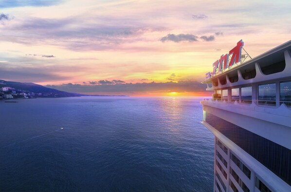 A cruise ship with a balcony overlooking a sunset over the ocean.