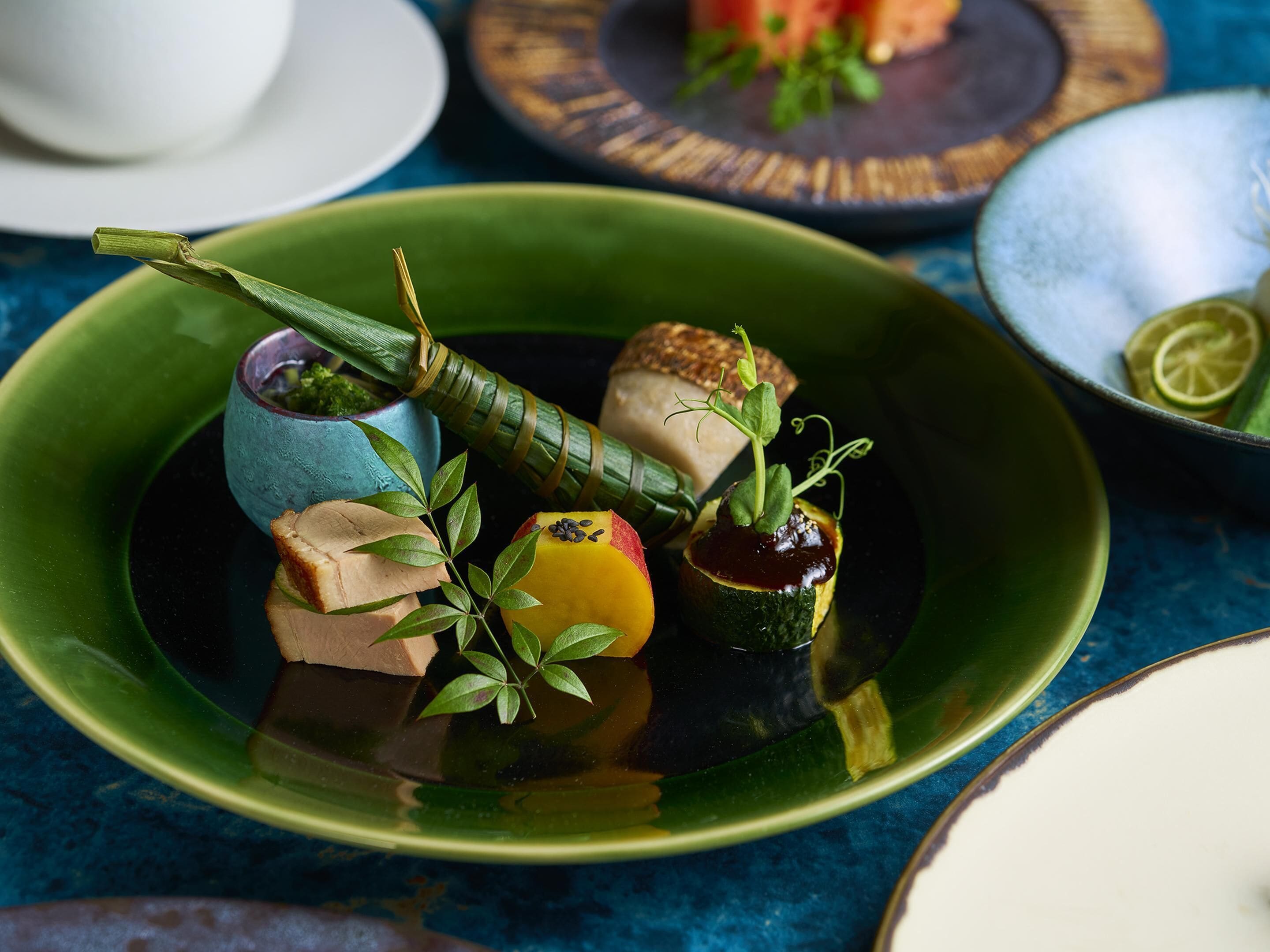 A green plate with food items, a blue cup, and a lime slice on a blue surface.