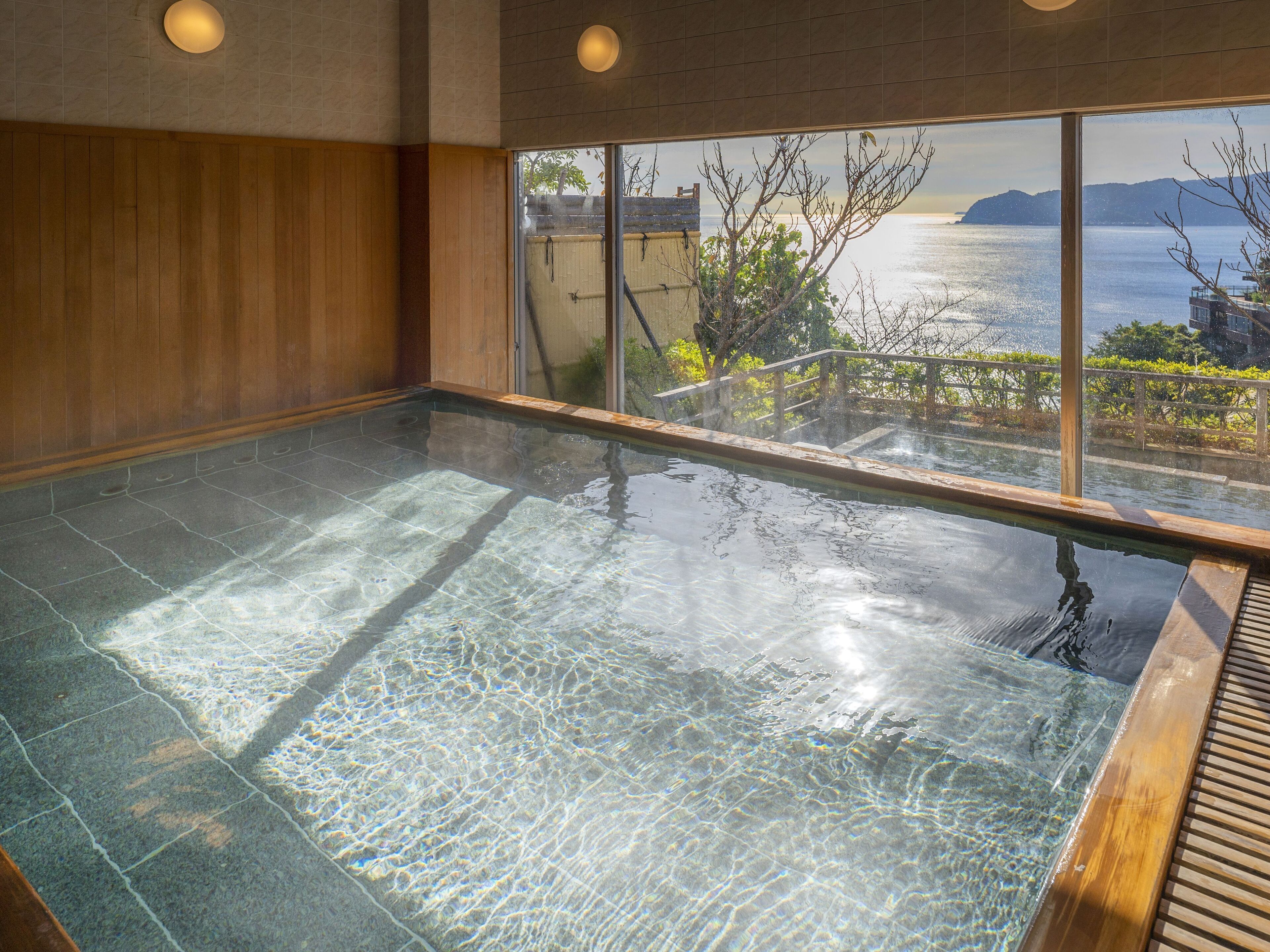 A clear indoor swimming pool with a view of the sea and hills.