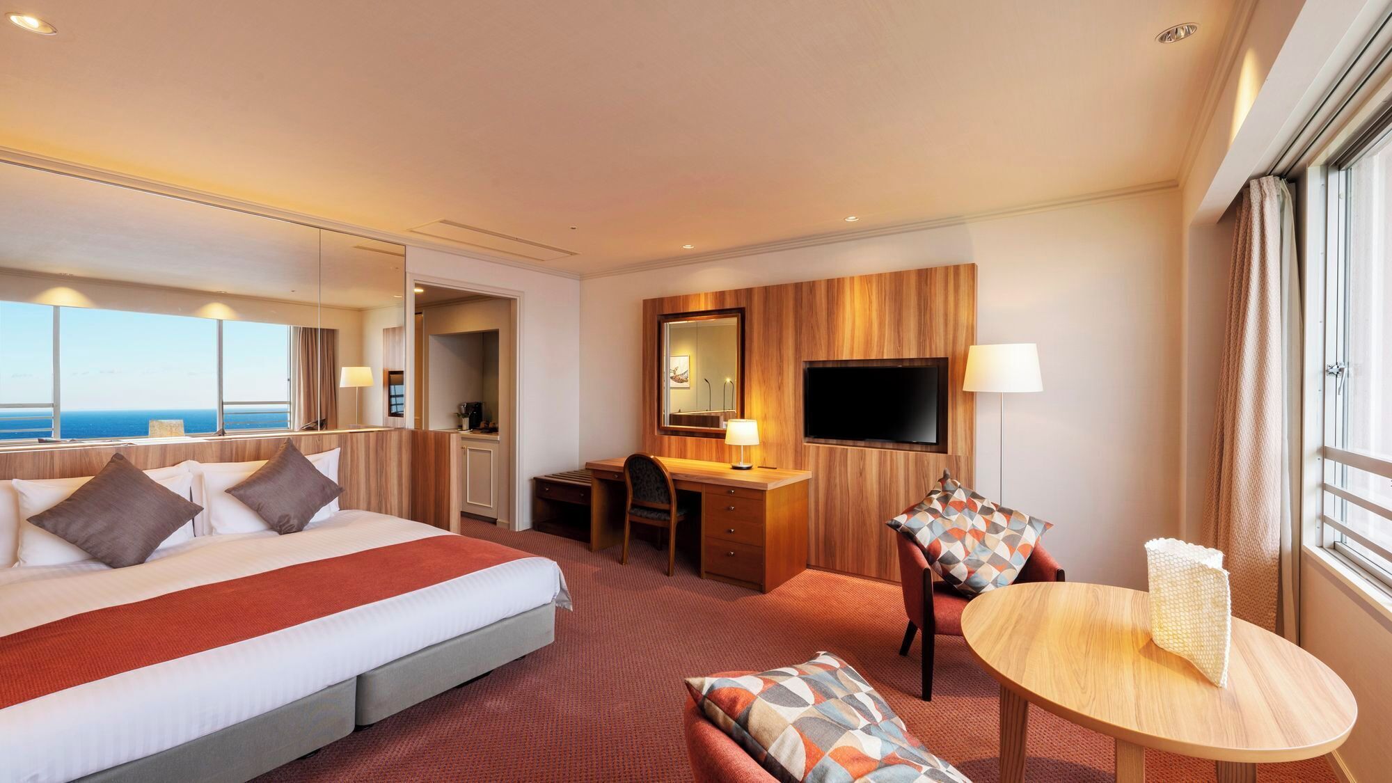 Habitación de hotel con cama, escritorio, silla, televisor y vista al mar.