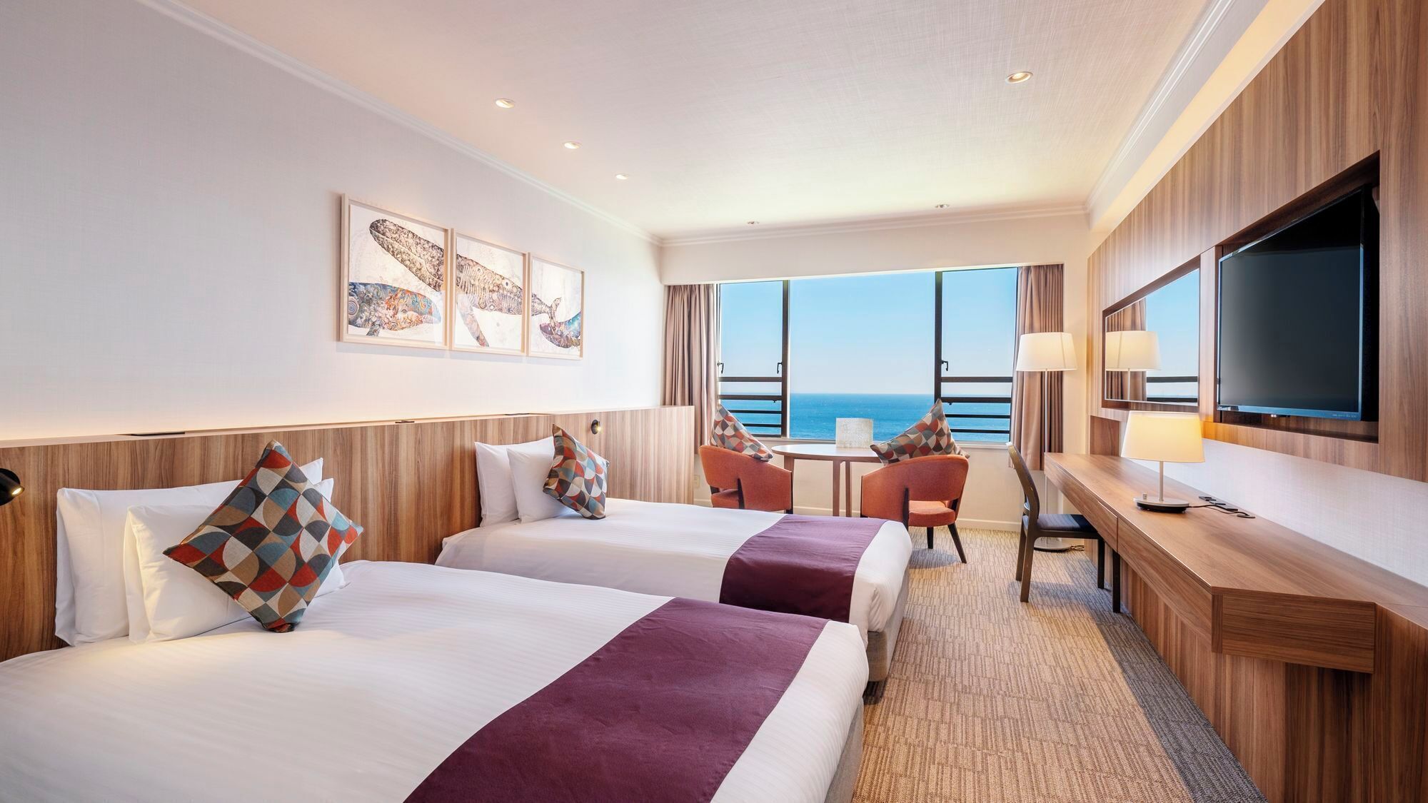 Habitación de hotel con dos camas, un escritorio, televisión y vista al mar.