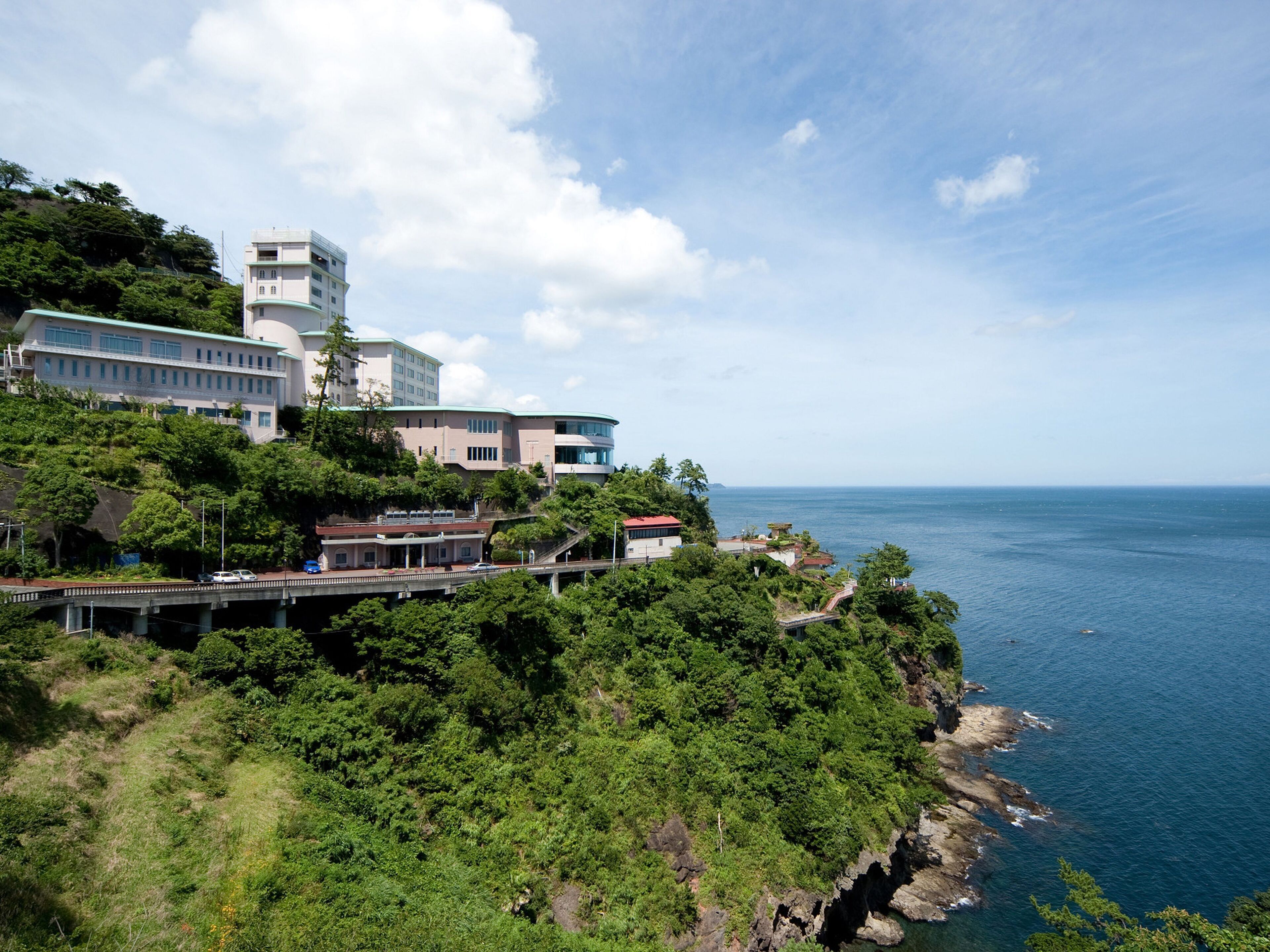 Un hotel frente al mar con varias construcciones, un puente y abundante vegetación.