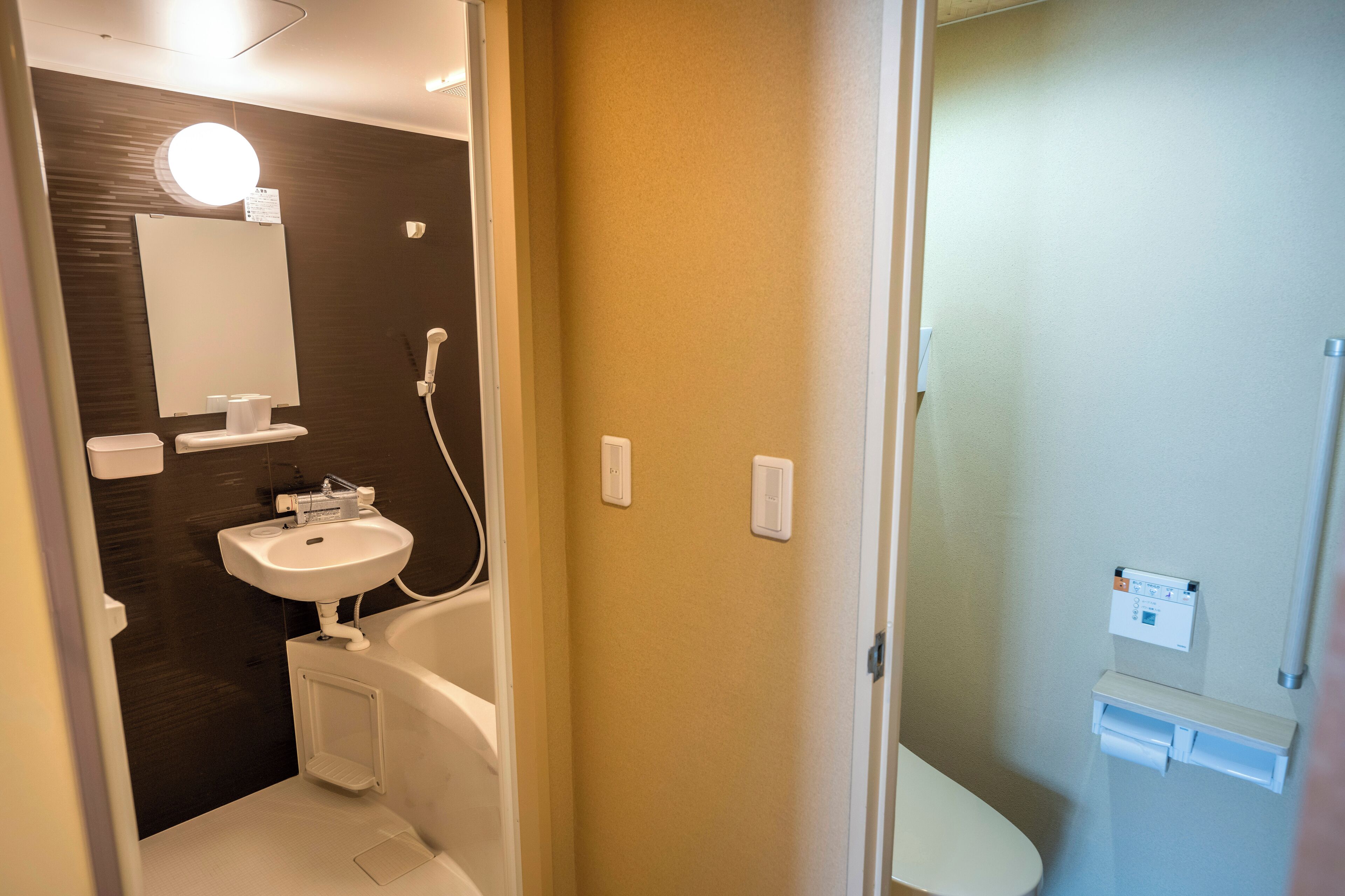 A bathroom with a white sink, mirror, and toilet. There is a shower area with a control panel.