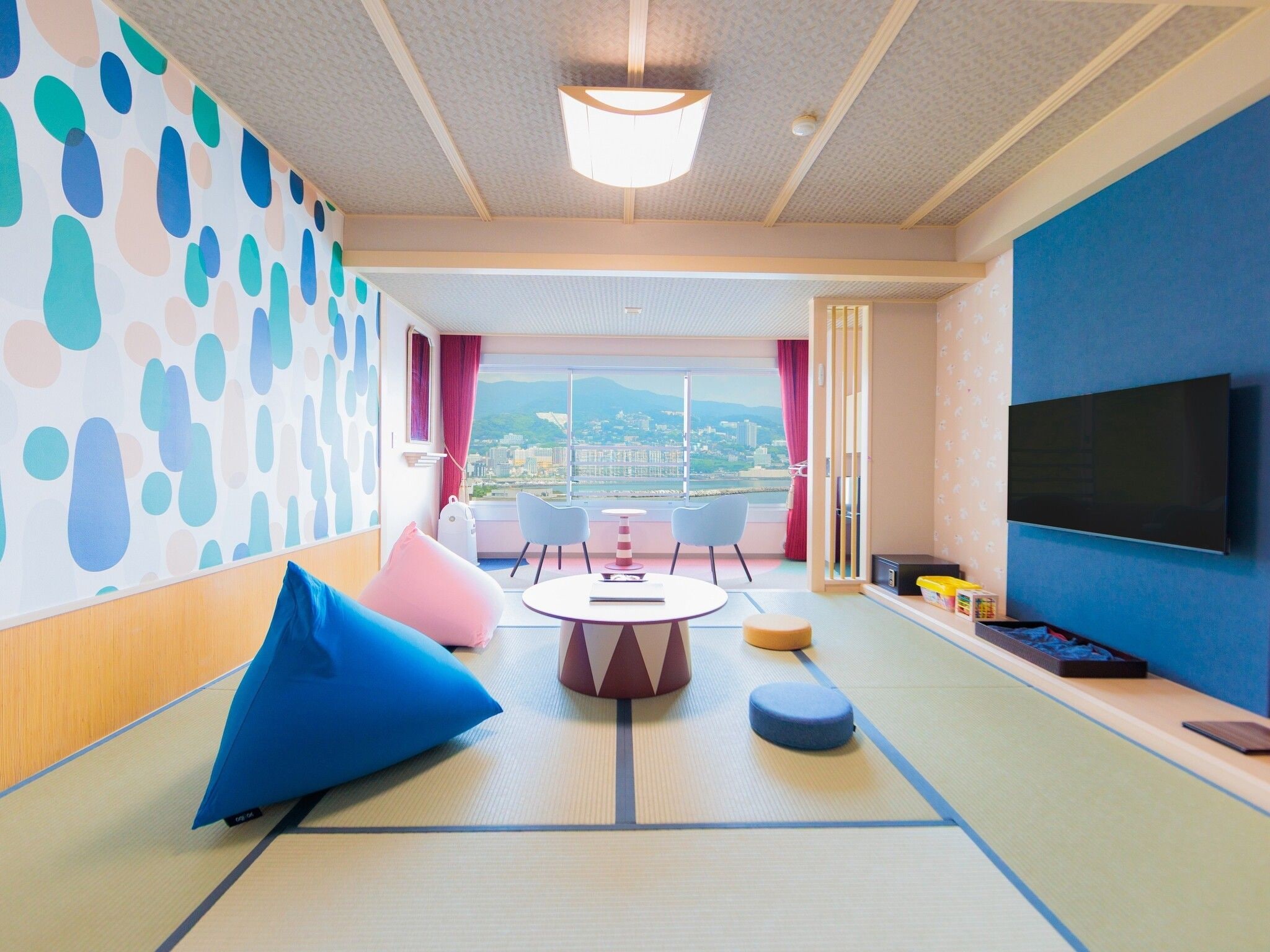 A modern hotel room with a large window, a round table, and a flat-screen TV.