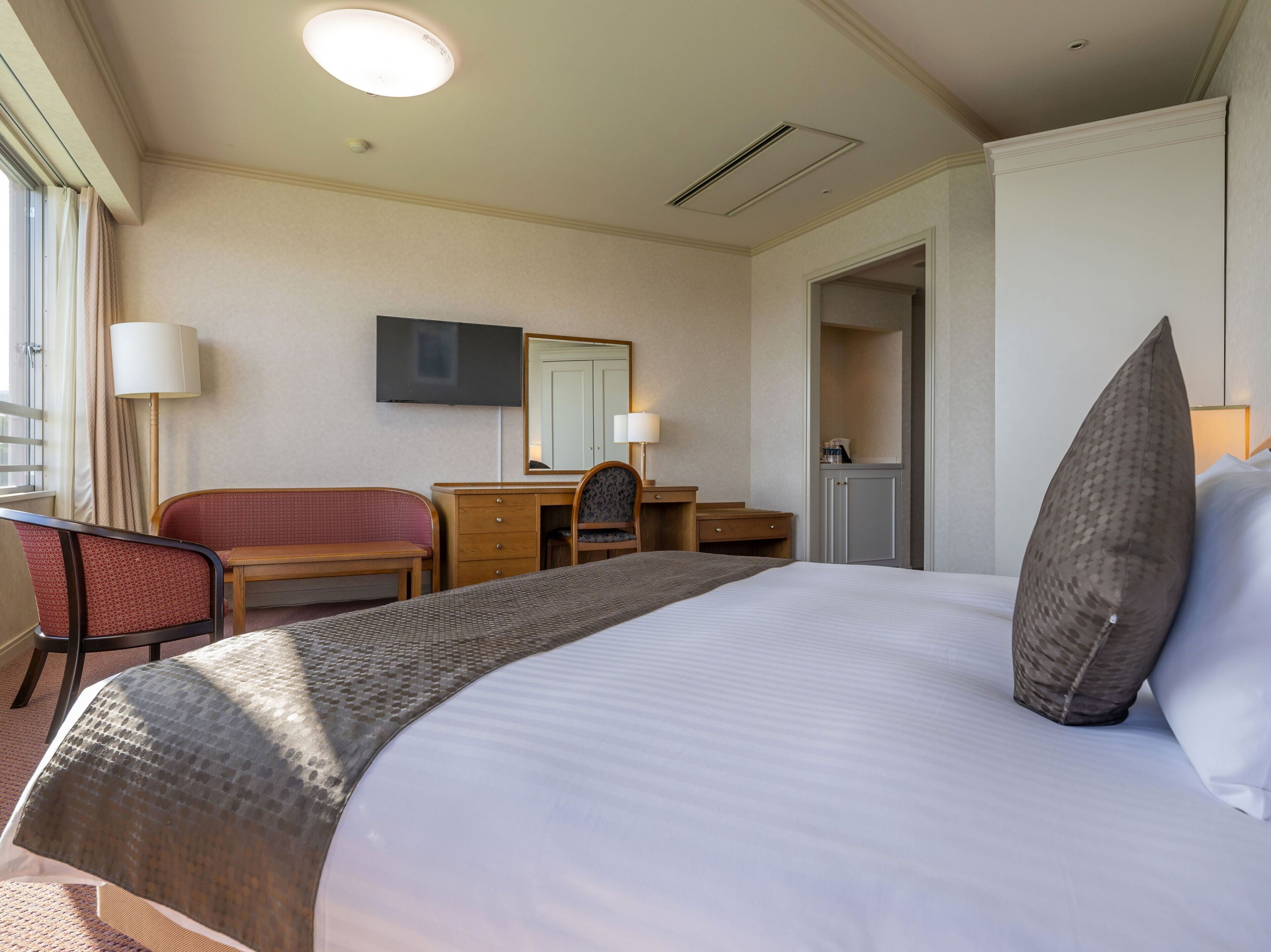 Une chambre d’hôtel avec un grand lit, un bureau, une chaise, une télévision et une armoire.