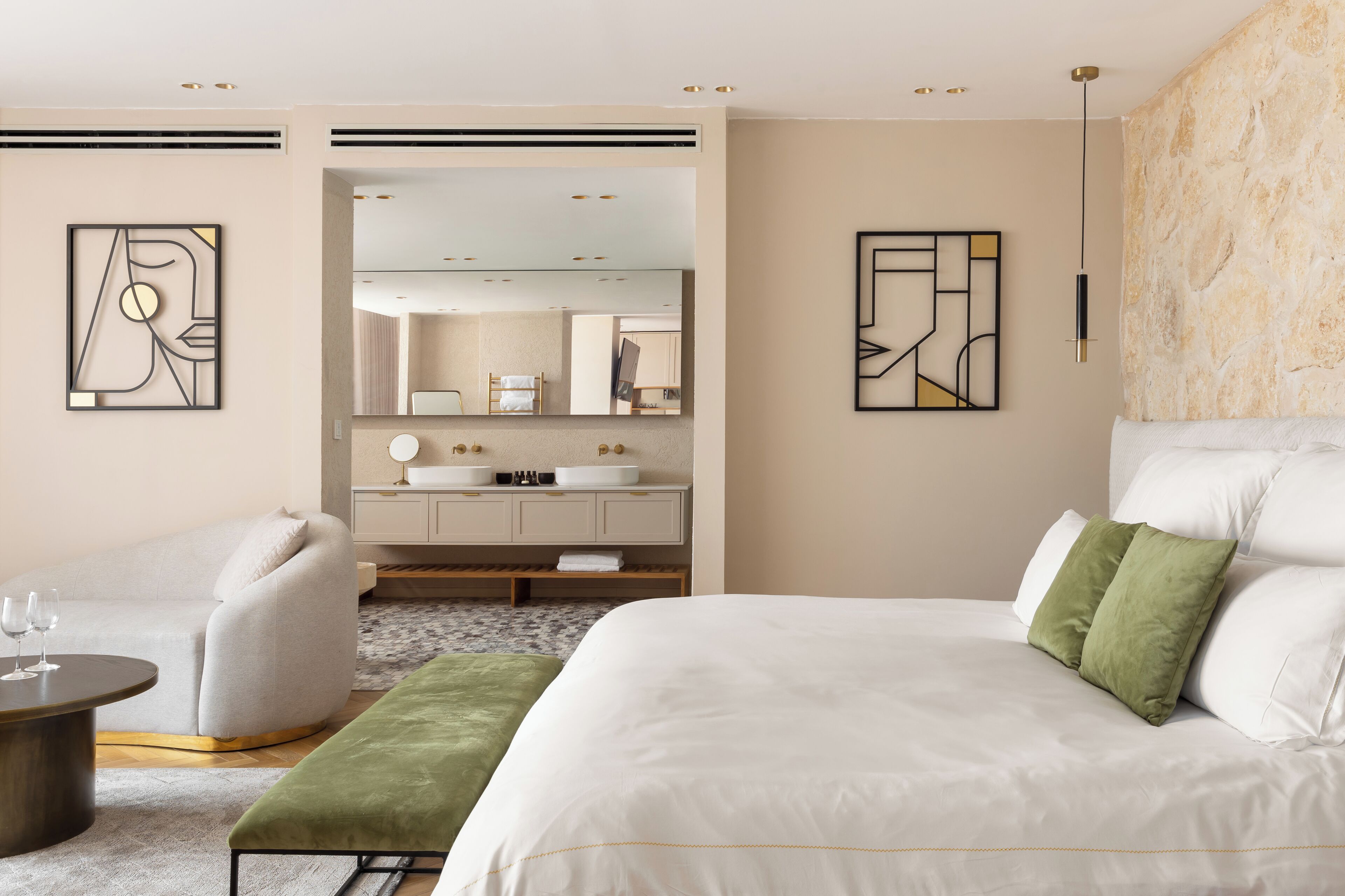 A modern hotel room with a large bed, a sofa, a small table, and a bathroom visible through an open door.