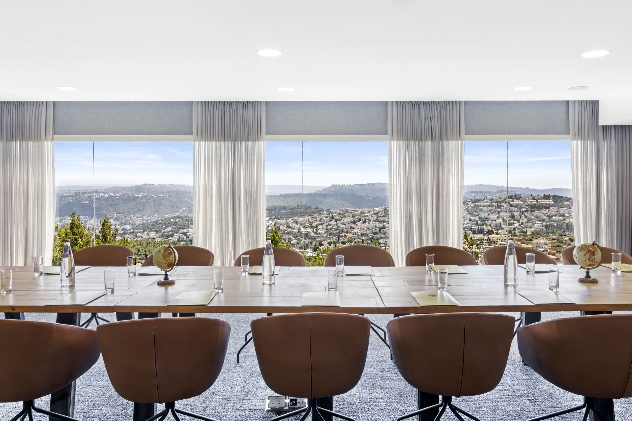 A conference room with a panoramic city view, large windows, and a long table with chairs.
