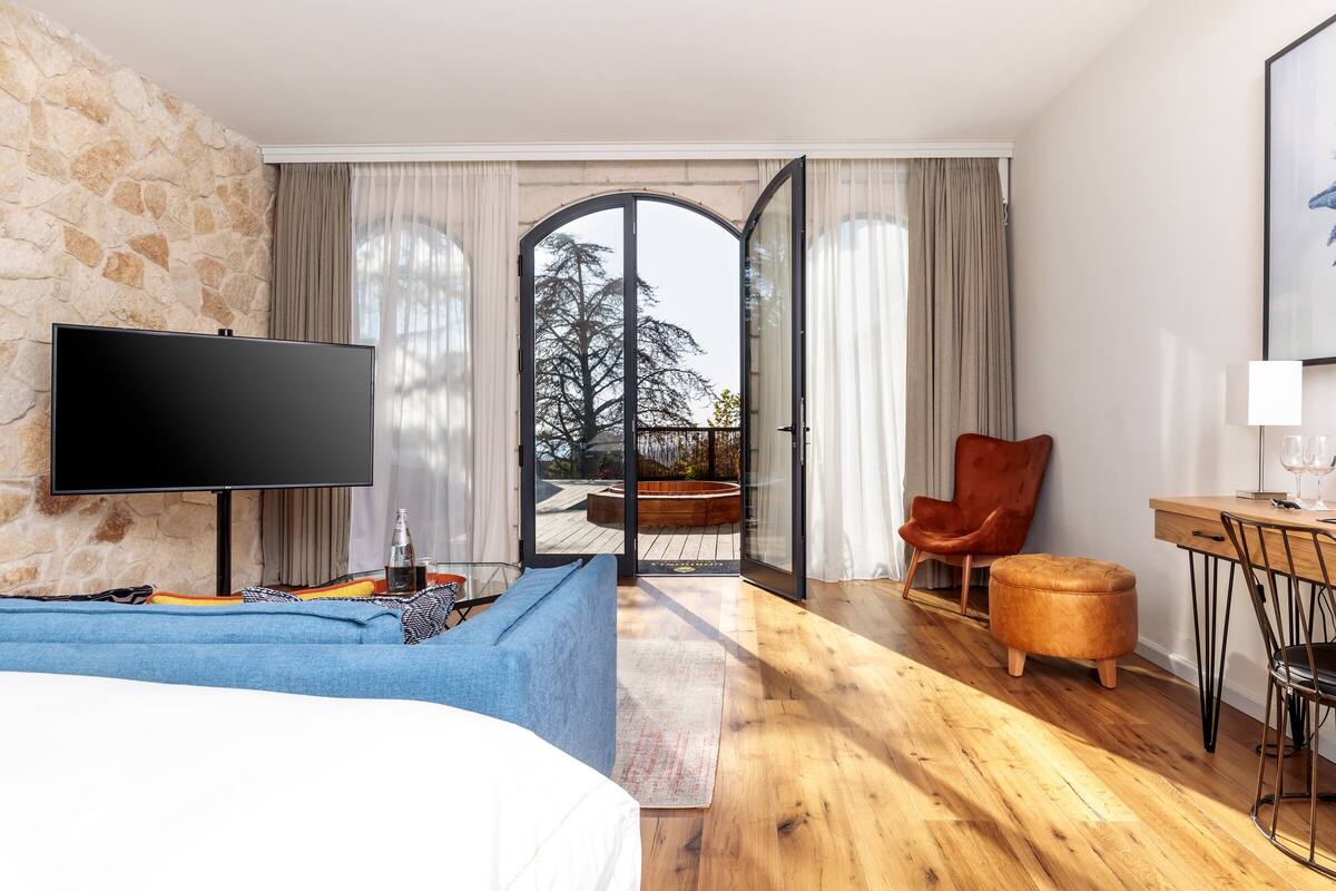 Une chambre d’hôtel moderne avec un mur en pierre, un téléviseur à écran plat, un canapé bleu, une table à manger en bois et une chaise rouge.
