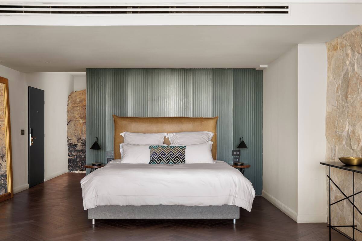 Une chambre moderne avec un grand lit, un mur d’accent en pierre et un design minimaliste.