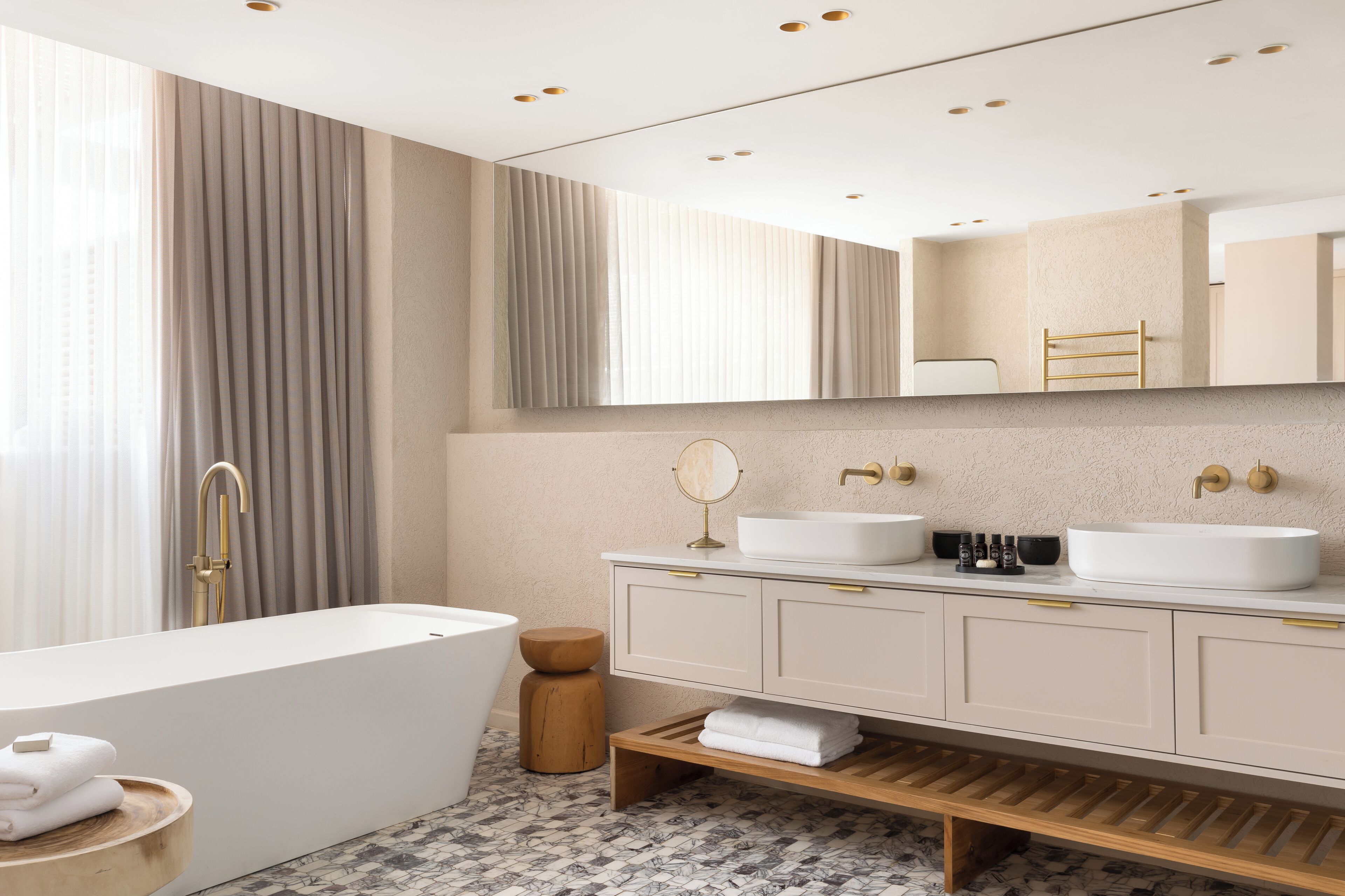 Un baño moderno con una bañera independiente, dos lavamanos, un mueble de tocador con tiradores dorados y un espejo grande.
