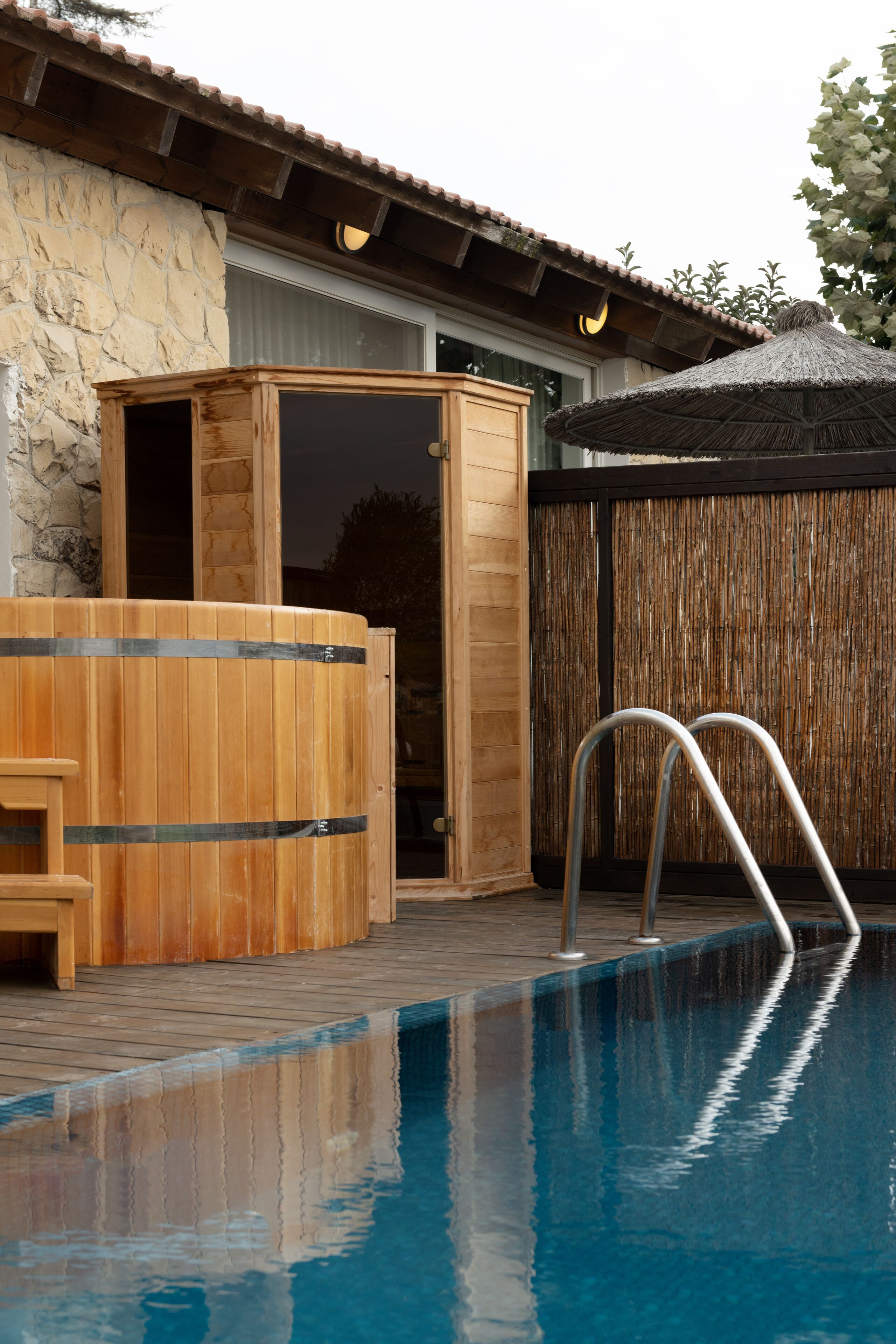 Un espace piscine doté d’un jacuzzi en bois, d’une terrasse en bois et d’une clôture en bambou.