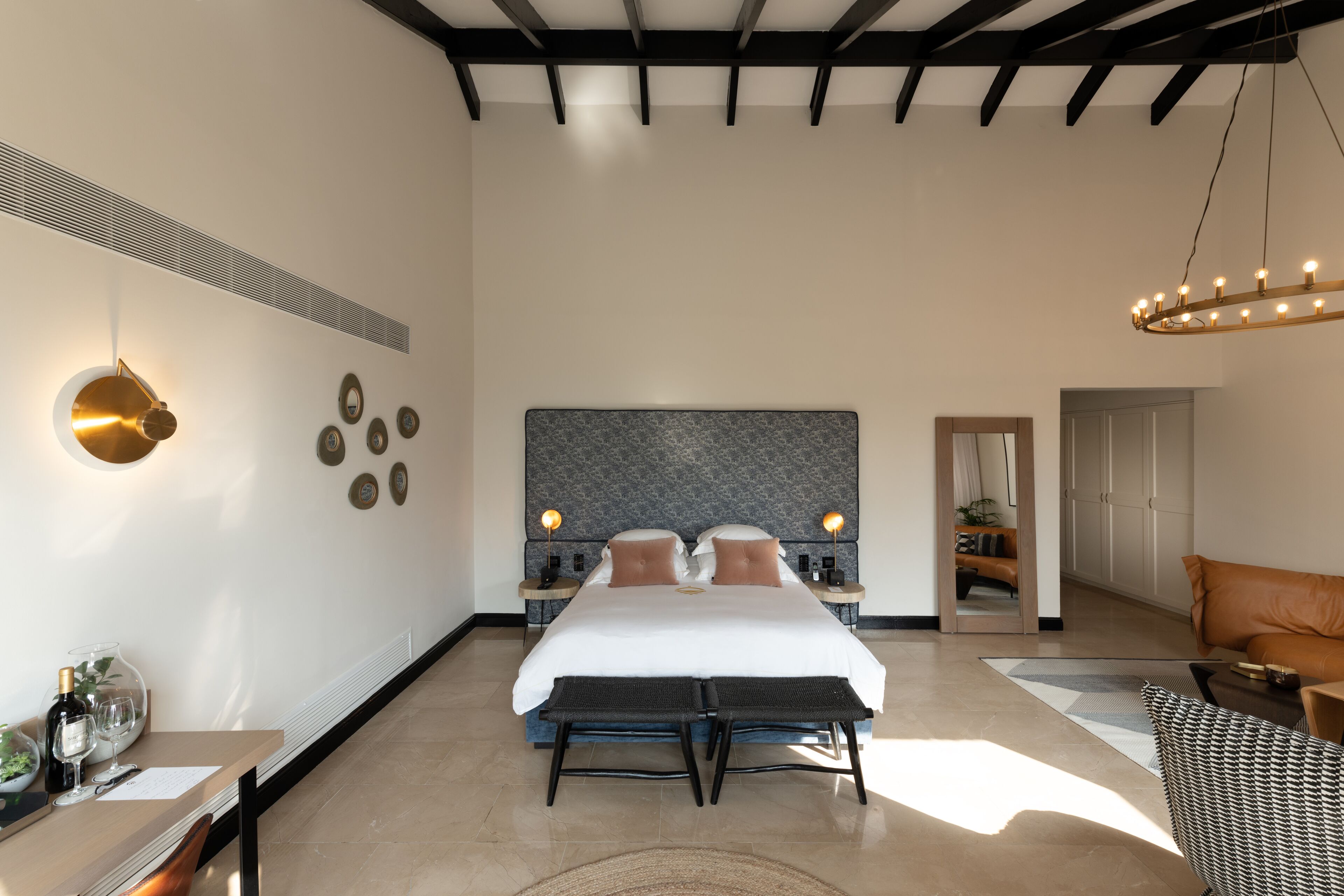 A modern hotel room with a large bed, bedside tables, a chandelier, and a view of the hallway.