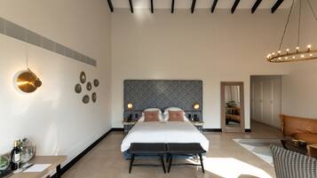 A modern hotel room with a large bed, bedside tables, a chandelier, and a view of the hallway.