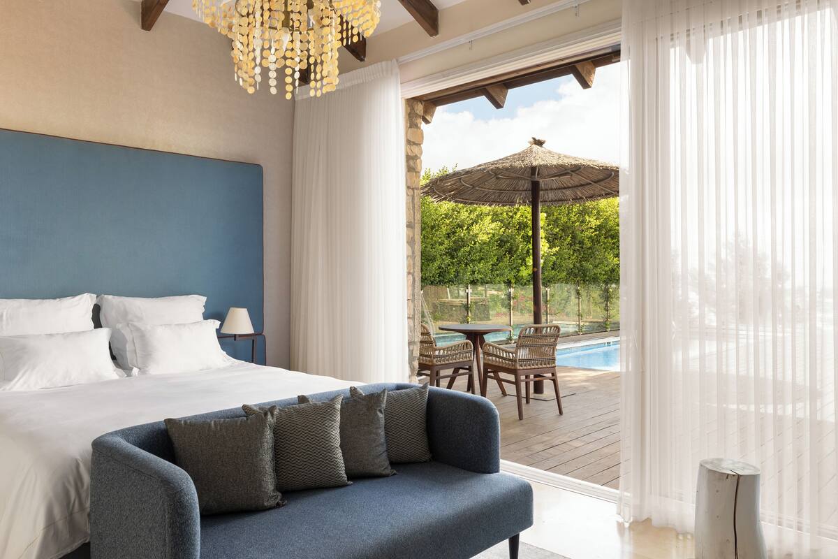 Une chambre avec un grand lit, un canapé bleu et une vue sur un espace piscine extérieur.