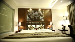A hotel room with a large bed, a headboard with a floral design, two bedside tables with lamps, and a chair. - JRD Exotica (New Delhi)