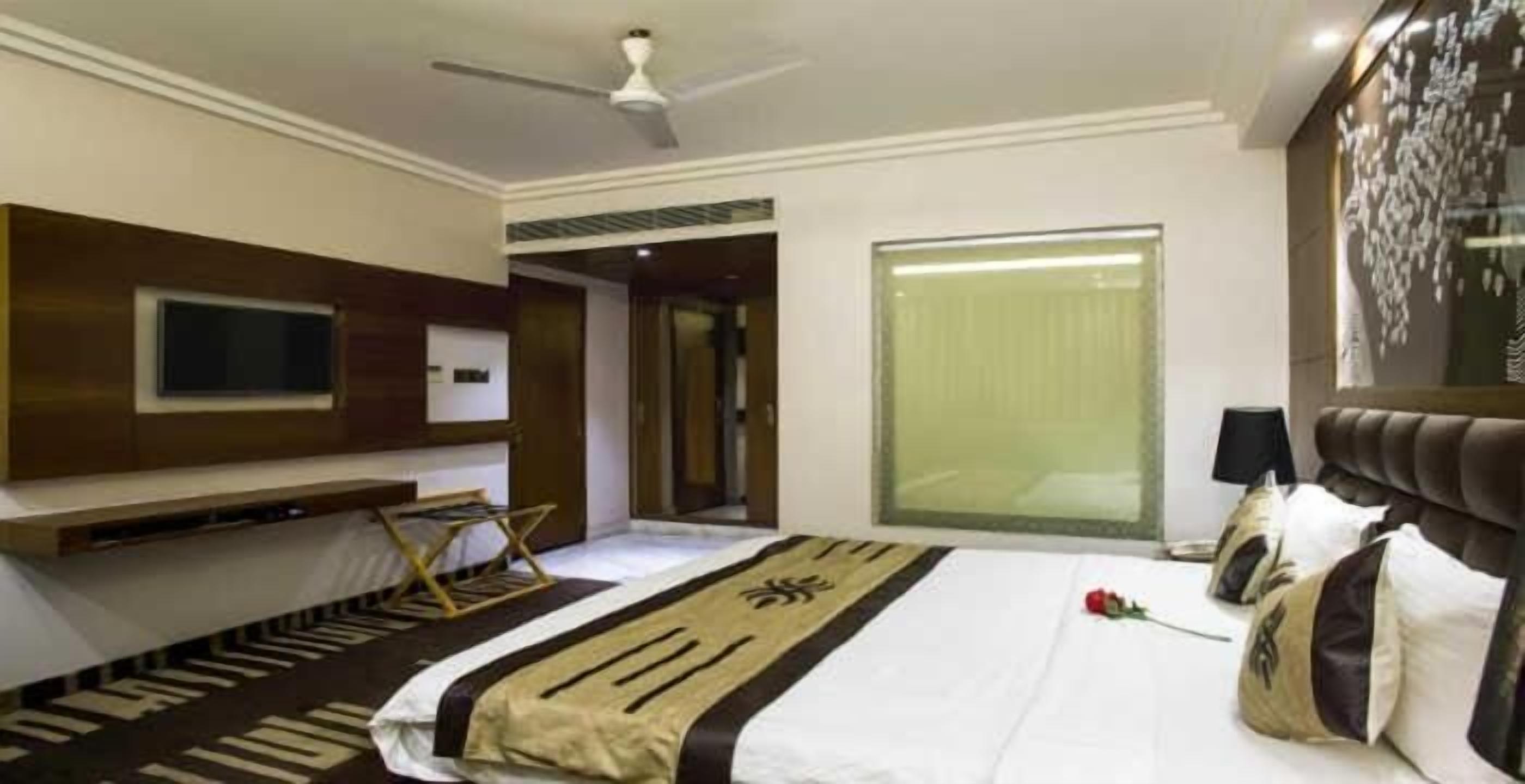 Habitación de hotel con una cama, un televisor de pantalla plana en la pared, un ventilador de techo y un ventanal con vistas.