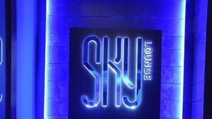 A neon sign reading "SKY LOUNGE" in a modern, dimly lit room with a wooden floor and two candelabras with flowers. - JRD Exotica (New Delhi)