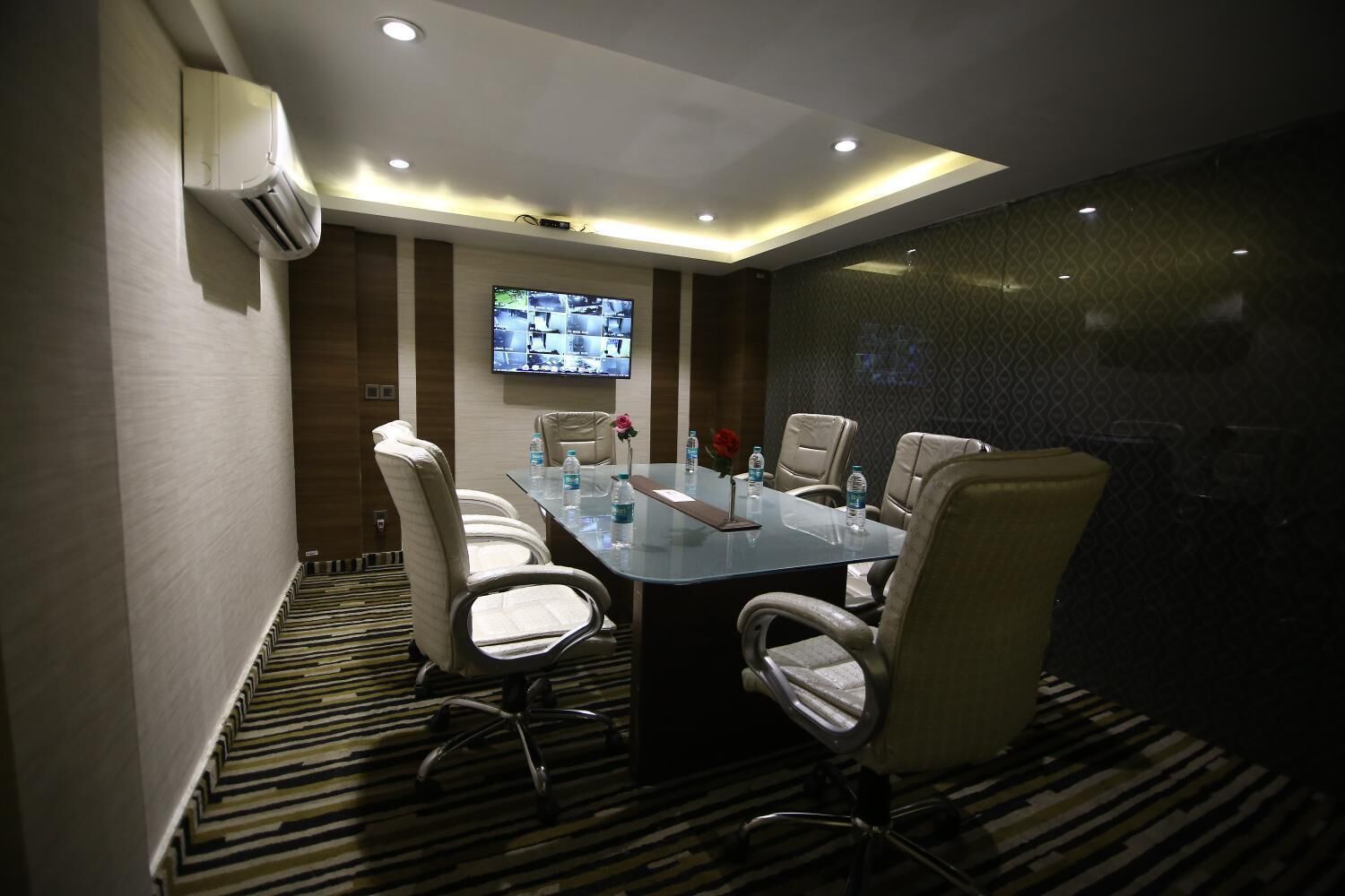 A conference room with a long table, six chairs, a flat-screen TV, and an air conditioning unit on the wall.
