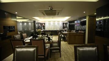 A modern dining area with a central table, surrounded by leather chairs, and a bar area with a TV screen.