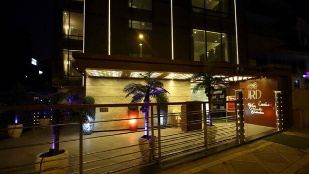 A modern building with a well-lit entrance, a sign reading "JRD," and a palm tree in the foreground. - JRD Exotica (New Delhi)