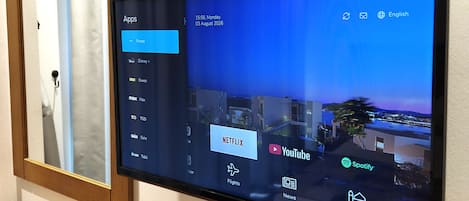 A flat-screen TV mounted on a wall displaying a digital interface with app icons, including Netflix, YouTube, and Spotify.