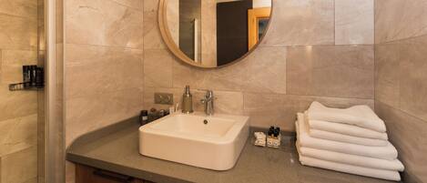 A bathroom with a sink, mirror, and towel stack.