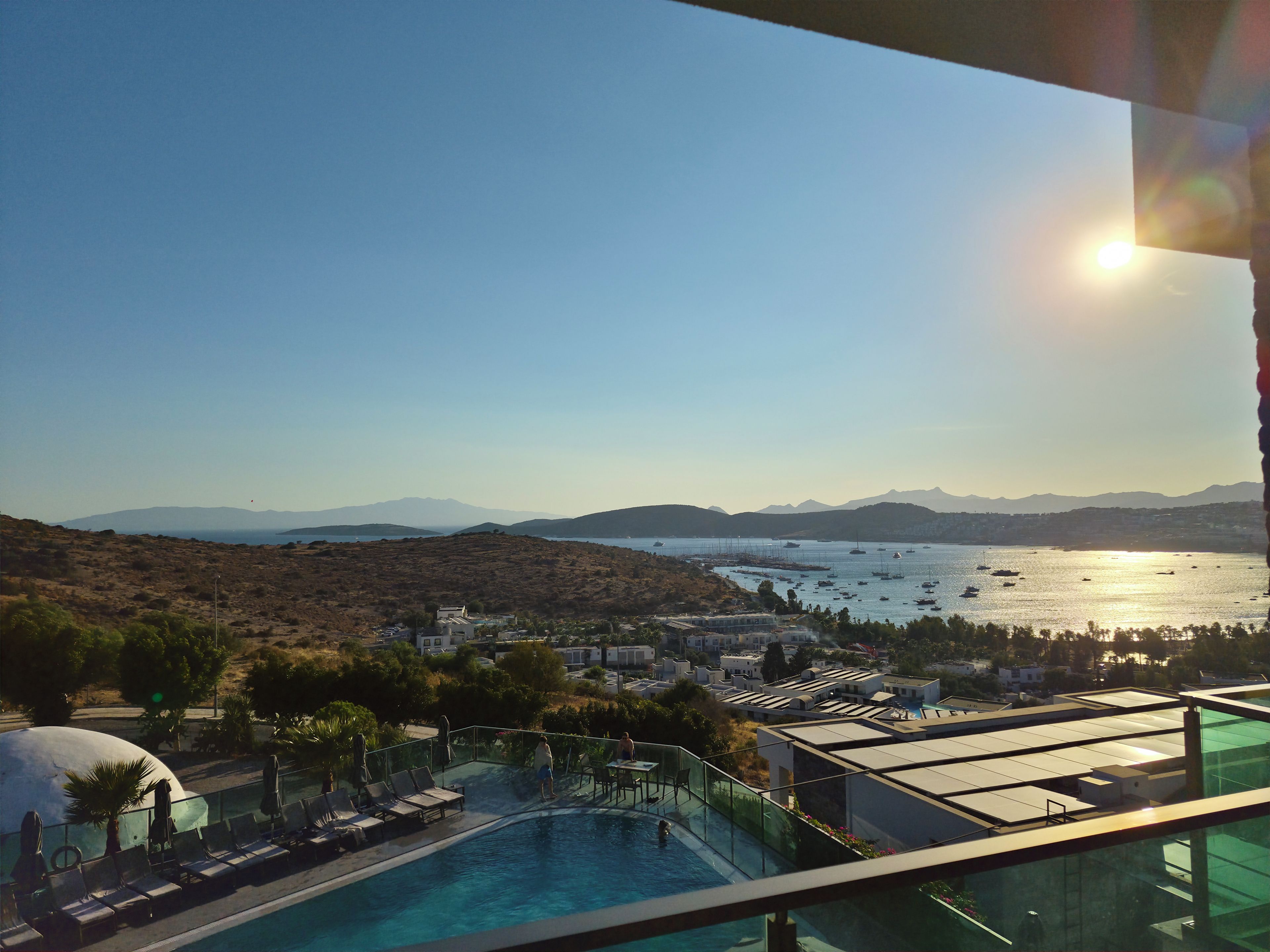 A pool area with lounge chairs and a view of the sea and mountains.