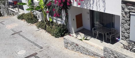 A modern building with a stone facade, a patio area with outdoor seating, and a garden with bougainvillea flowers.