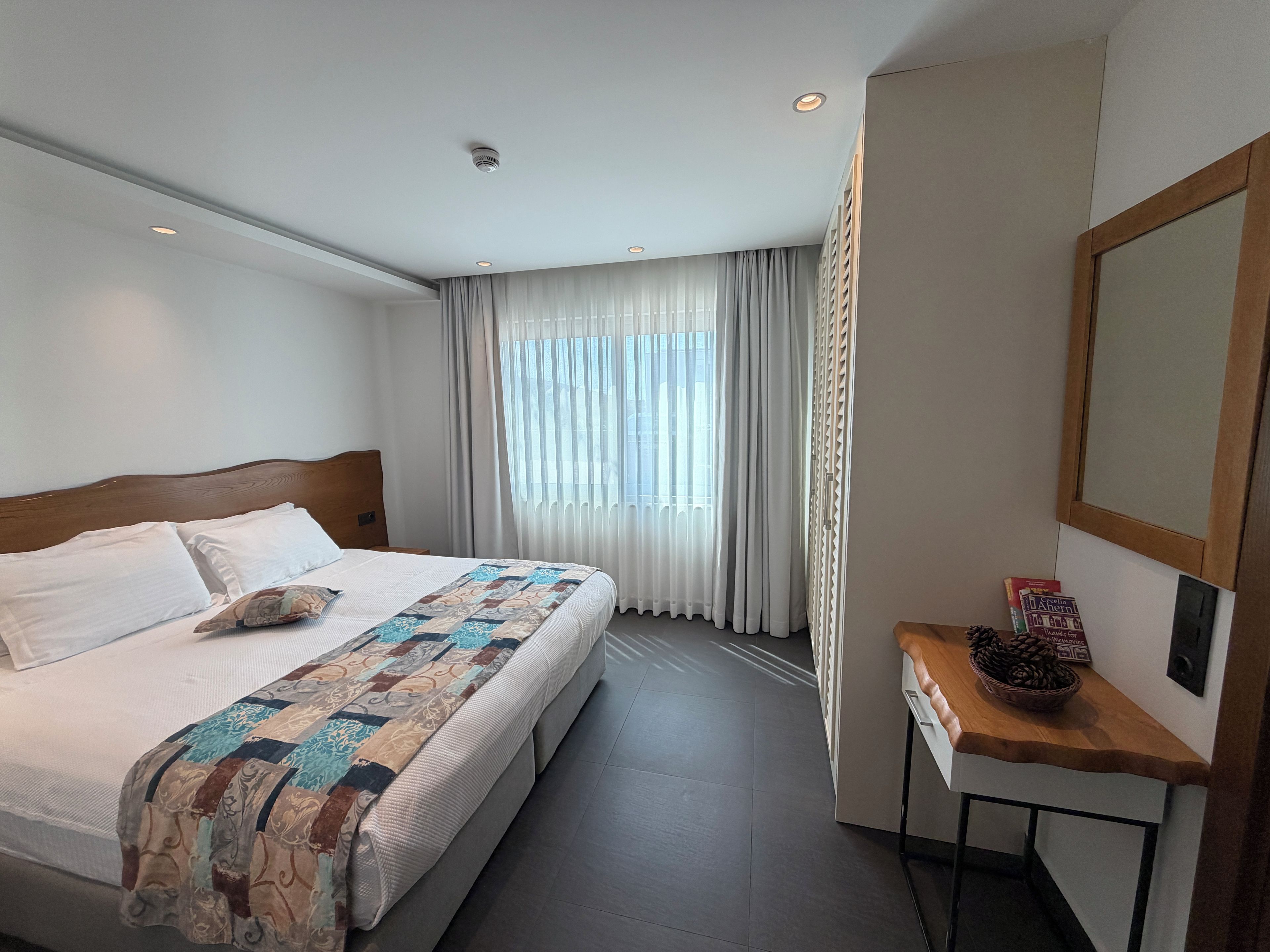 Een hotelkamer met een groot bed, een nachtkastje, een spiegel en een raam met gordijnen.