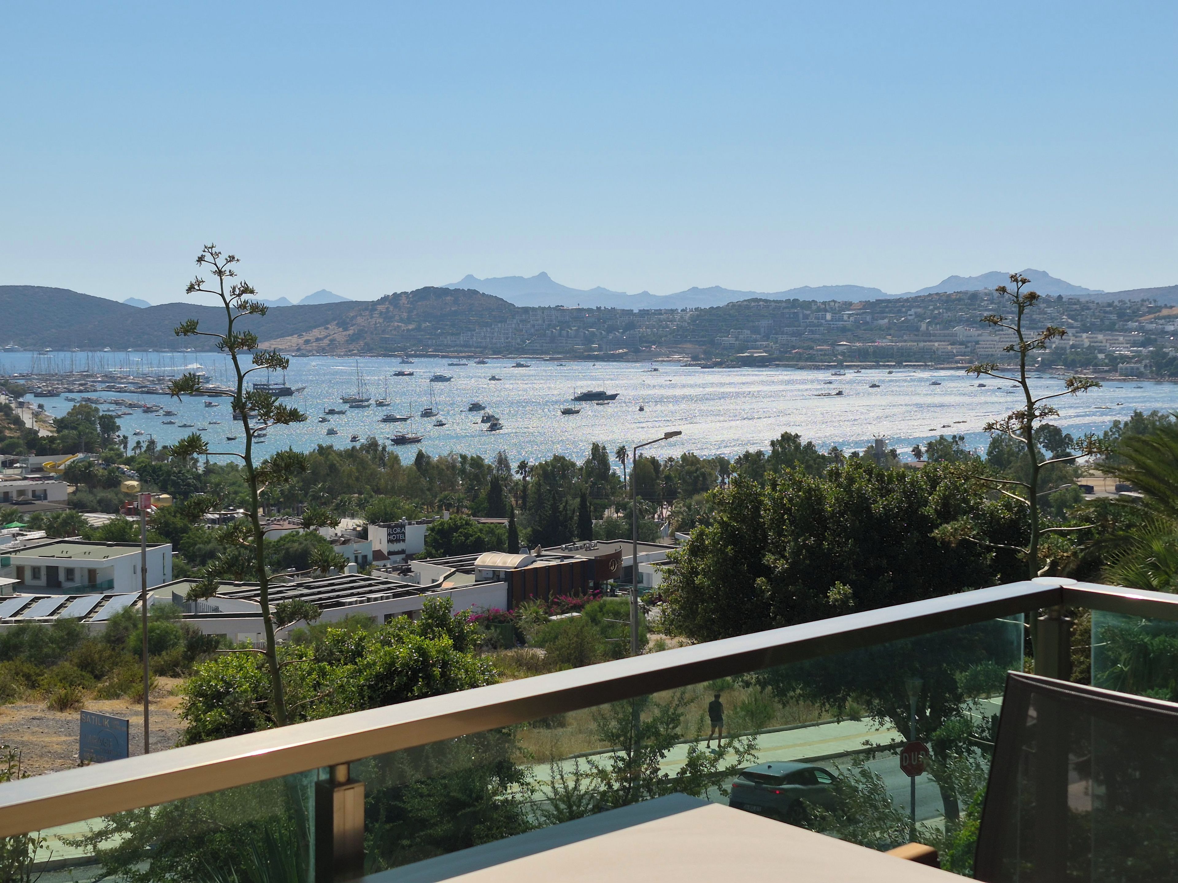 Vista costera con un puerto deportivo, edificios y una cordillera al fondo.