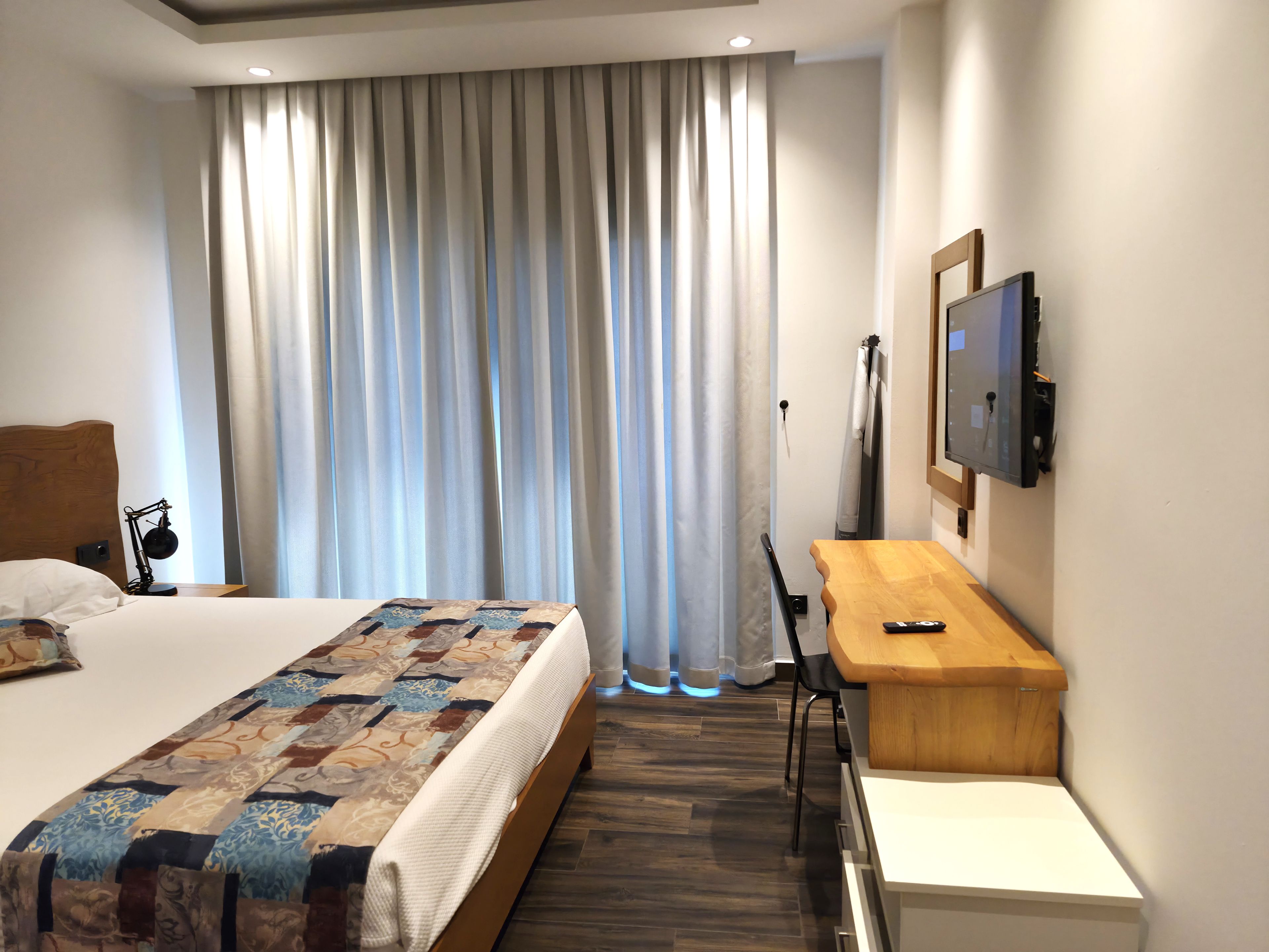Una camera d'albergo con un letto, una scrivania, una sedia, un televisore e una finestra con tende.