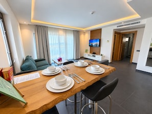 A modern hotel room with a dining area, a sofa, a TV, and a view of the outdoors. - Degirmenburnu Residence (Bodrum)