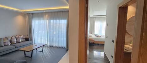 A modern living room with a sofa, a coffee table, and a view through a doorway to a bedroom.