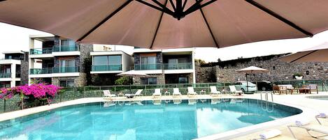 A swimming pool with lounge chairs and umbrellas, surrounded by multi-story buildings with balconies.