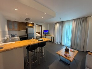 A modern hotel room with a kitchenette, a dining area, a small table with books, and a TV. - Degirmenburnu Residence (Bodrum)