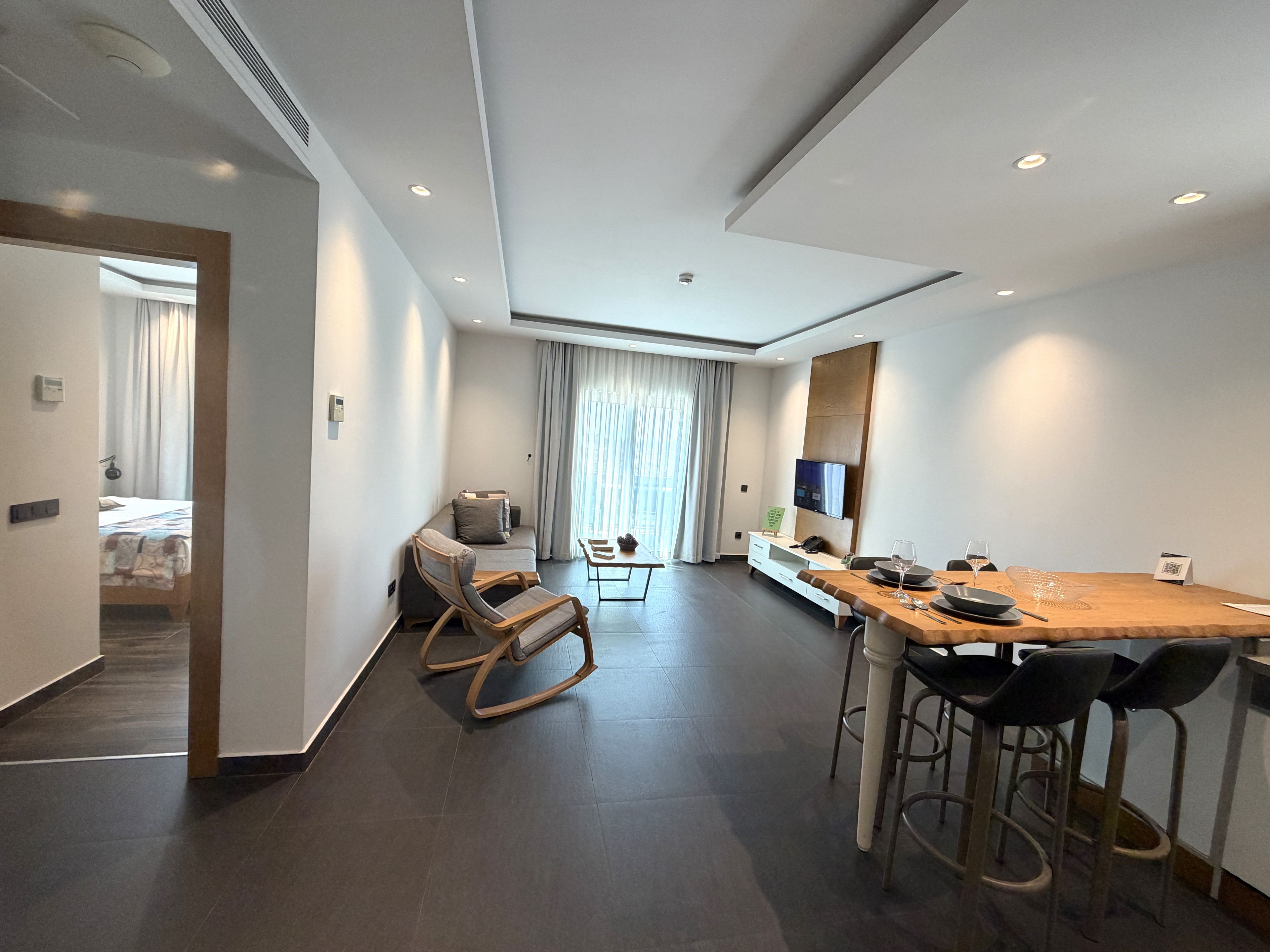 Une chambre d’hôtel moderne dotée d’un coin repas, d’un canapé, d’une télévision et offrant une vue sur l’extérieur.