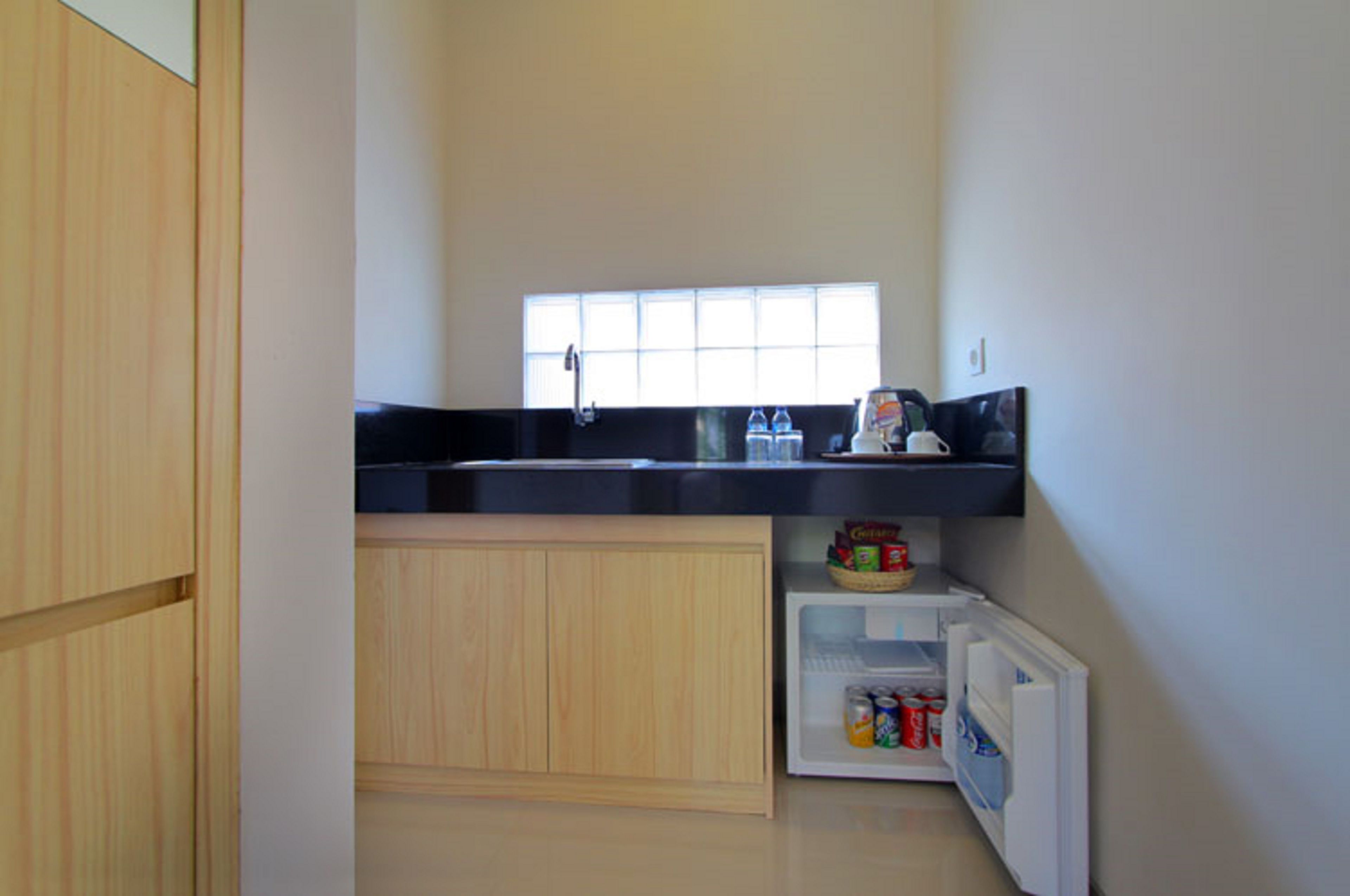 A compact kitchen with a black countertop, a window above the sink, and a small refrigerator below.