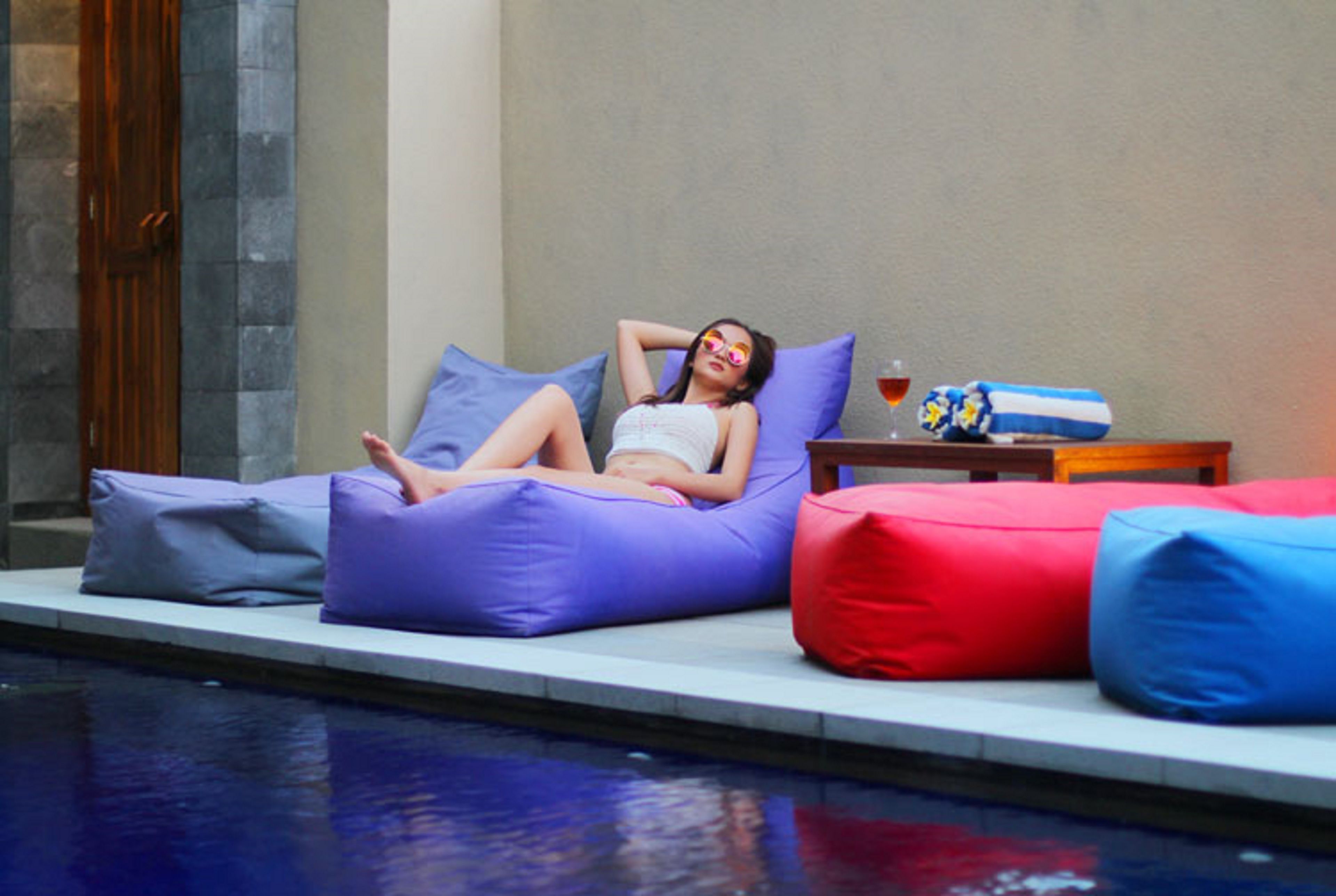 A person lounging on a purple bean bag chair by a poolside.