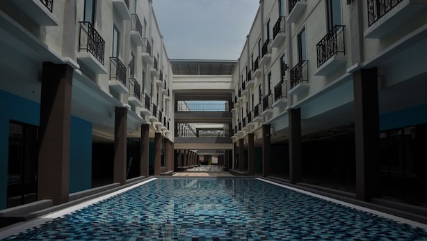 A large indoor swimming pool with a checkered tile floor, surrounded by multiple balconies with black railings. - Temasek Hotel (Malacca City)