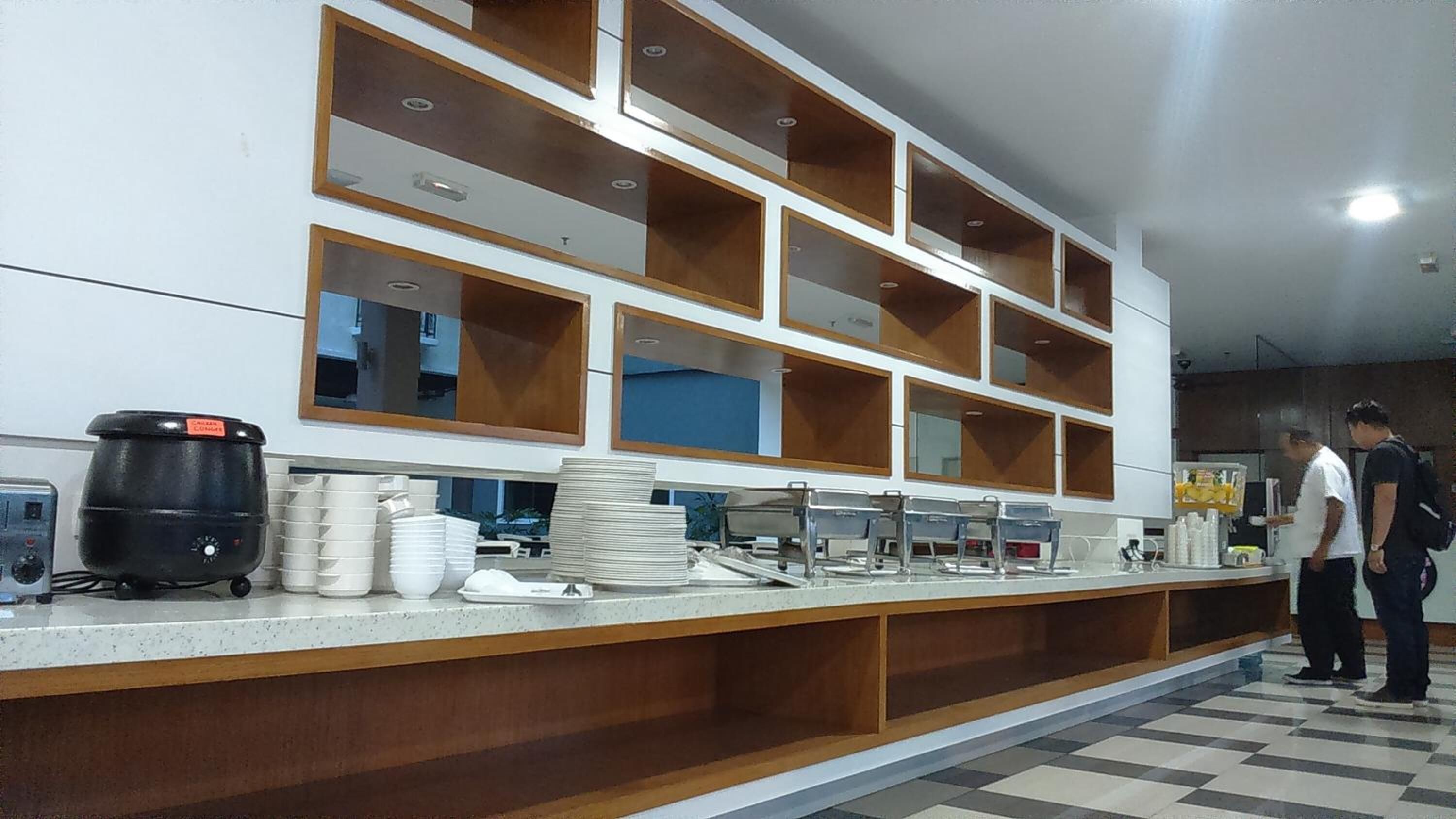 Uma cozinha com uma bancada comprida, diversos eletrodomésticos e prateleiras.