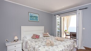 Ein Schlafzimmer mit einem Bett, einem Nachttisch, einer Lampe und Blick ins Freie durch eine Schiebetür.
