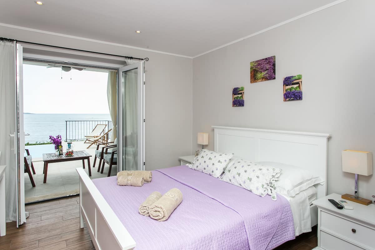 Une chambre d’hôtel avec un lit, une table de chevet, une table avec des chaises et une vue sur la mer, accessible par une porte coulissante.