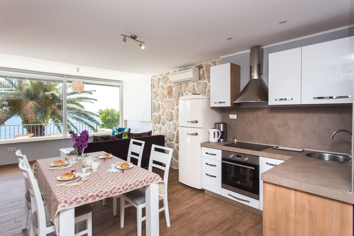 Une cuisine moderne avec des armoires blanches, un mur d’accent en pierre et un coin repas avec une table dressée pour deux personnes.