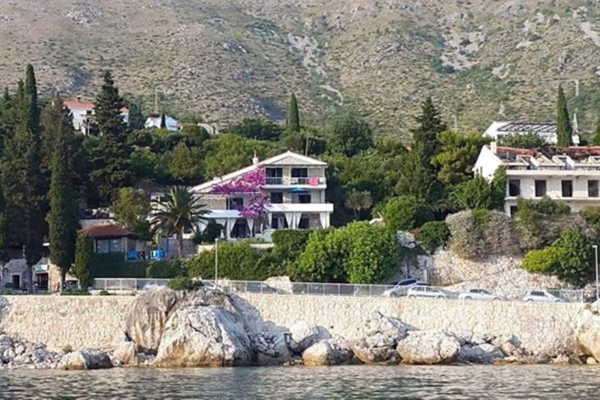 Une propriété située sur la côte, avec une grande maison entourée de verdure, un rivage rocheux et un paysage montagneux en arrière-plan.