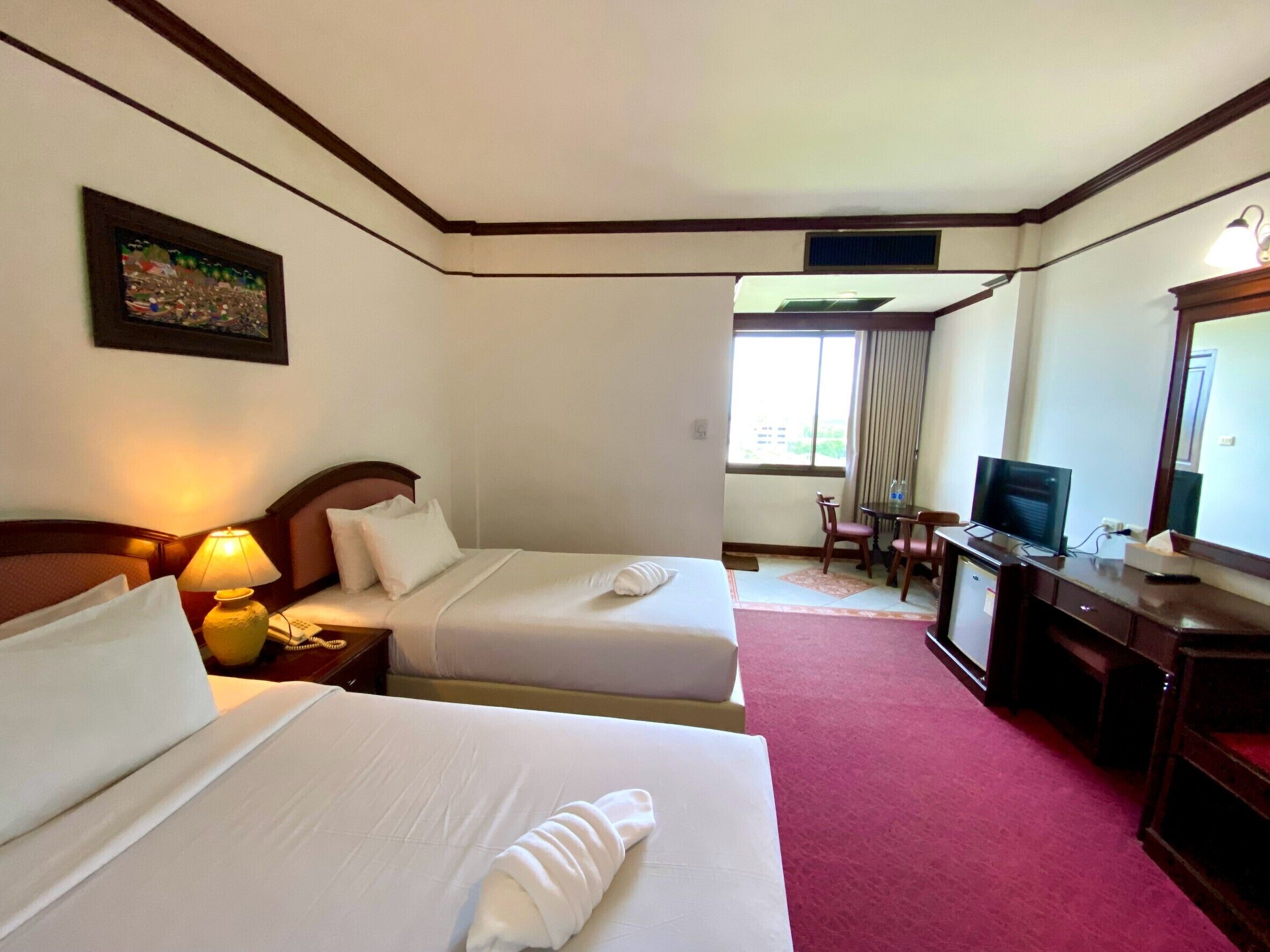 A hotel room with two beds, a desk with a television, and a window with curtains.