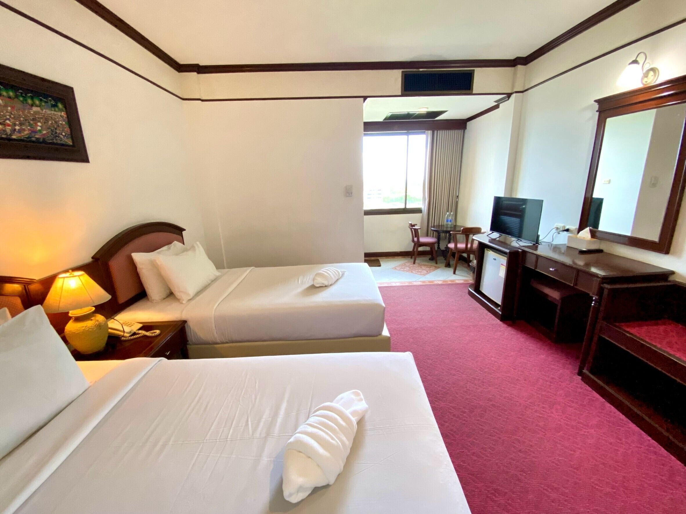A hotel room with two beds, a desk with a computer, a television, and a window with curtains.