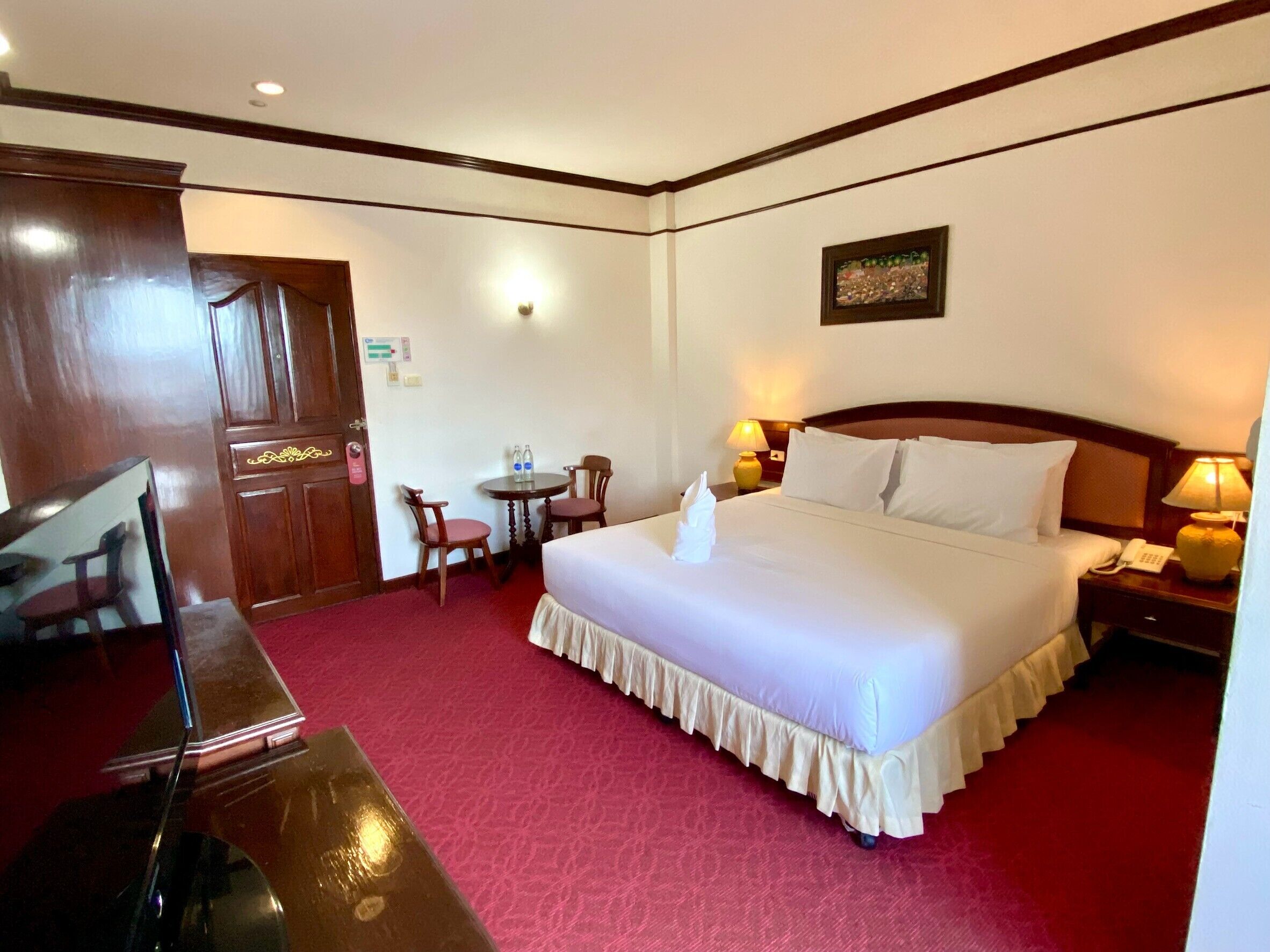 A hotel room with a large bed, a desk, a chair, a small table, and a painting on the wall.