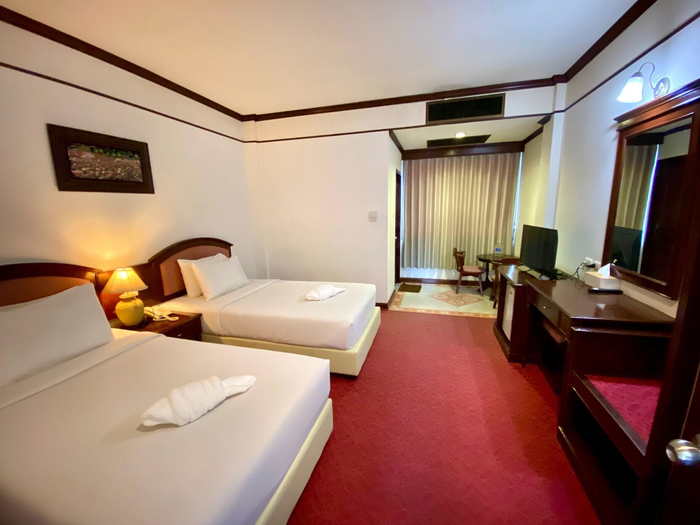 A hotel room with two beds, a desk, a chair, a television, and a window with curtains.