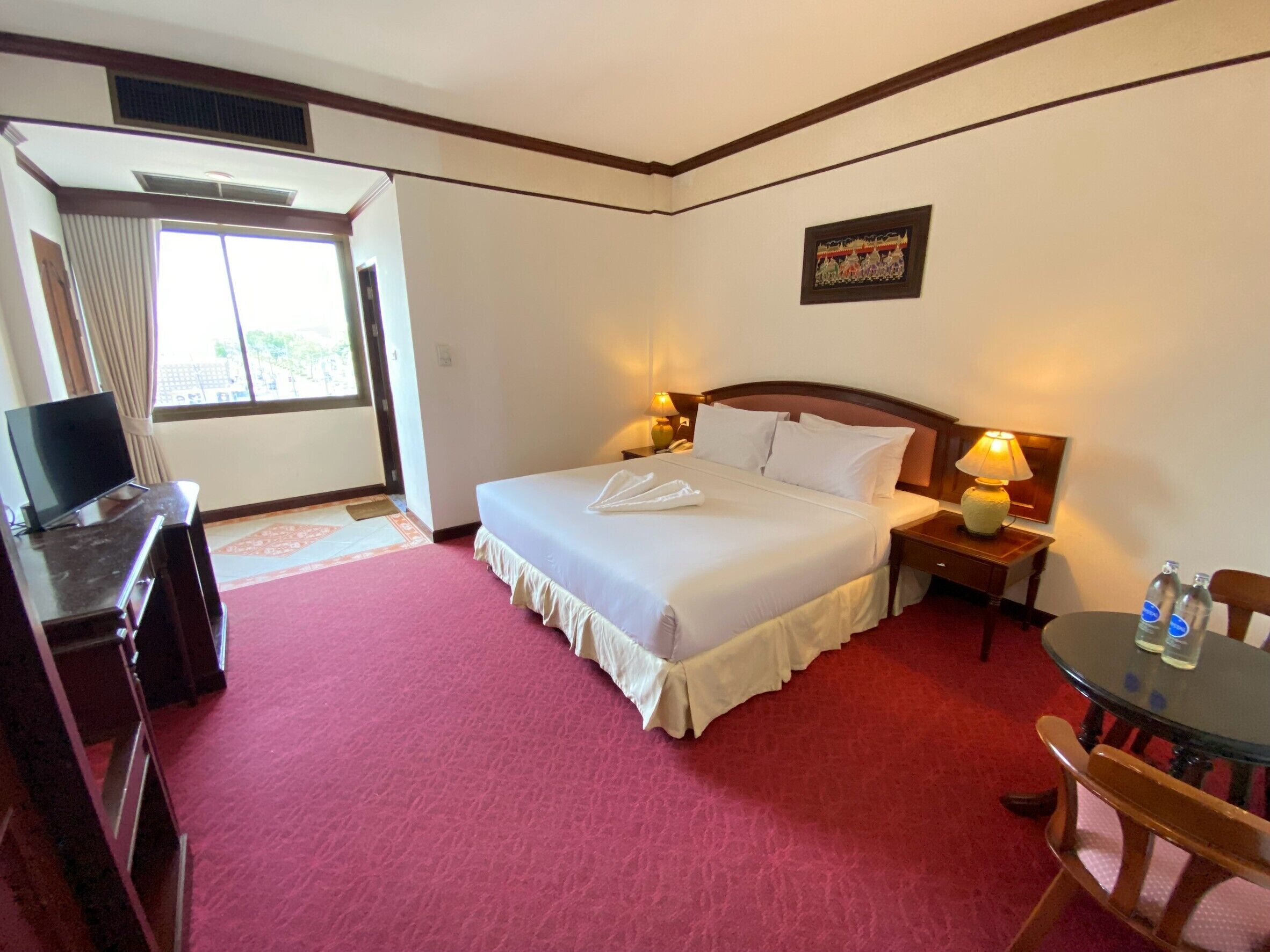 A hotel room with a bed, bedside lamps, a desk with a television, and a window with curtains.