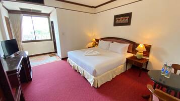 A hotel room with a bed, bedside lamps, a desk with a television, and a window with curtains.